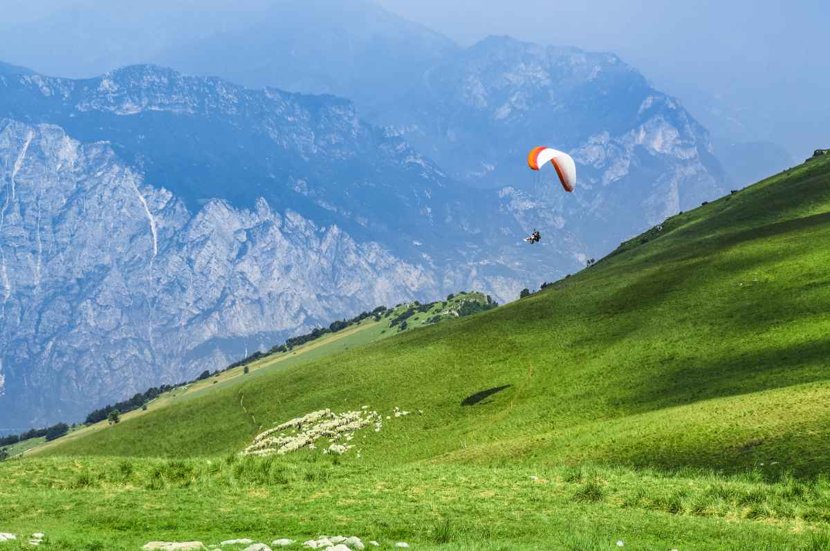 Paraglider against mountains and meadows, Monte Baldo, Lake Garda, Italy.